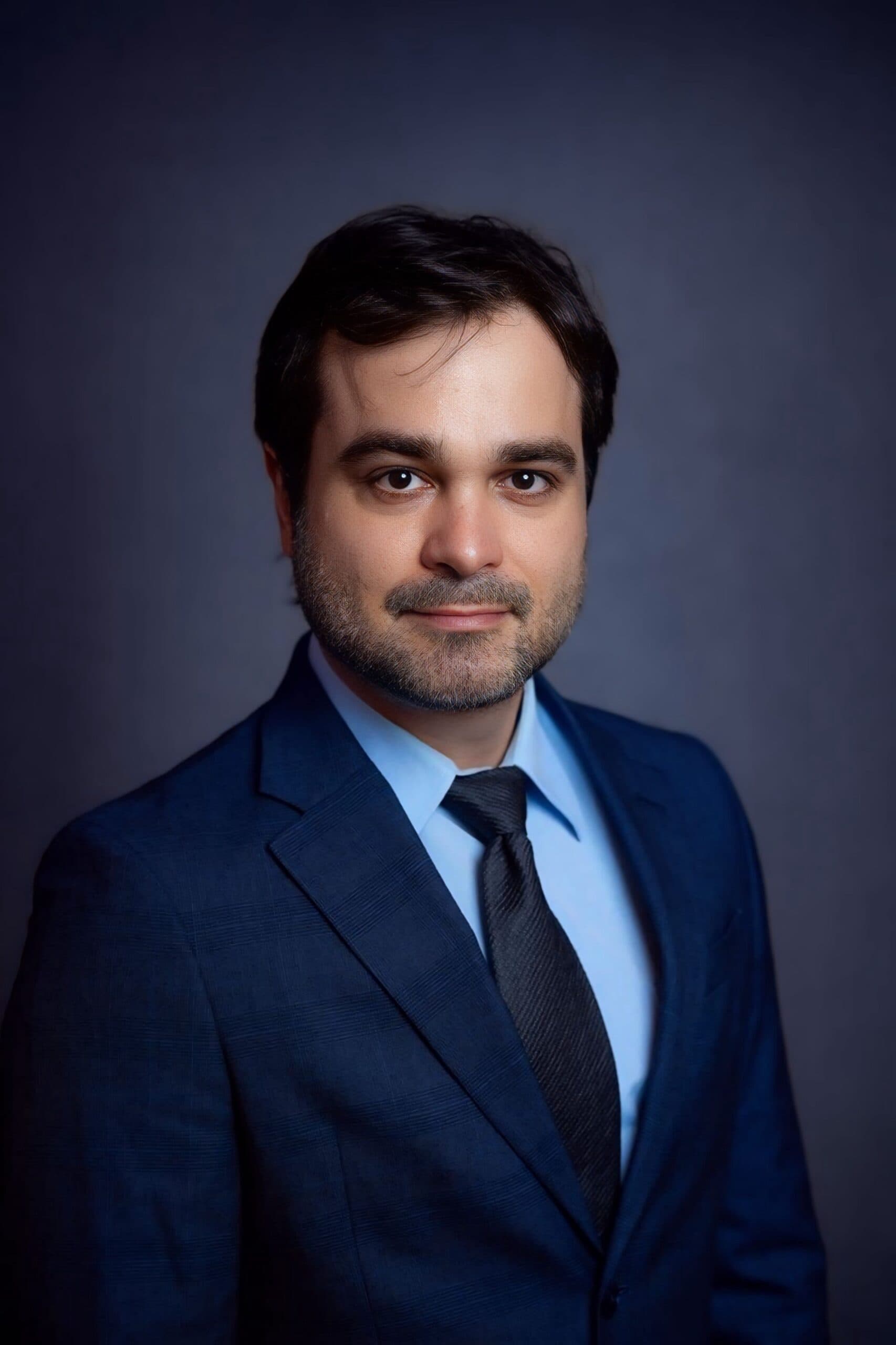 Carlos Gustavo Poggio headshot wearing a suit with a greyish dark blue background