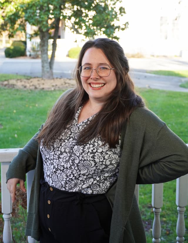 Berea College Admissions Counselor, Morgan Hudson Mecham, leaning against a white fence, with green grass and a tree in the background.