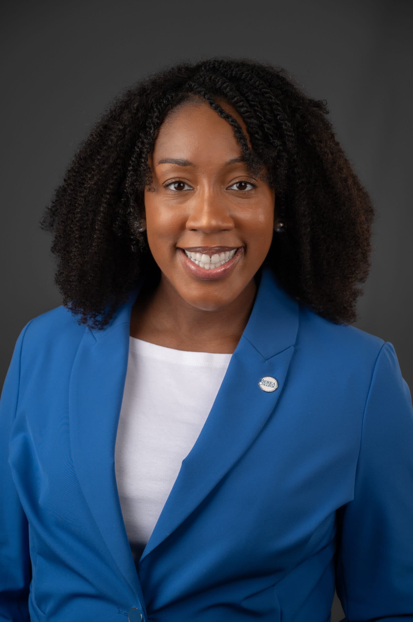 Olivia Coleman Dunn headshot with grey background and blue jacket and white shirt smiling
