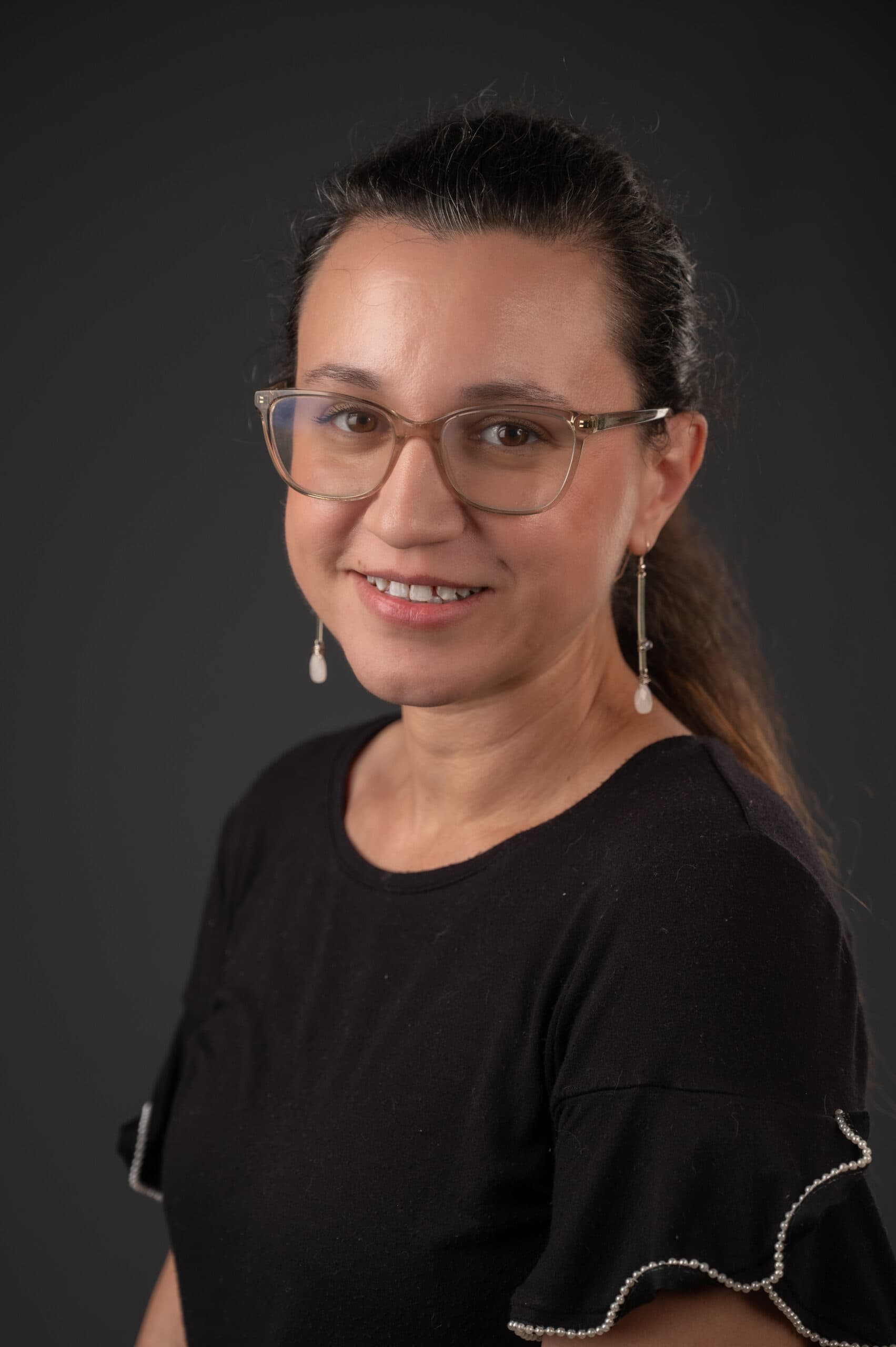 Jenny Boyle Akins headshot, sitting. Behind is a grey background and is wearing black smiling