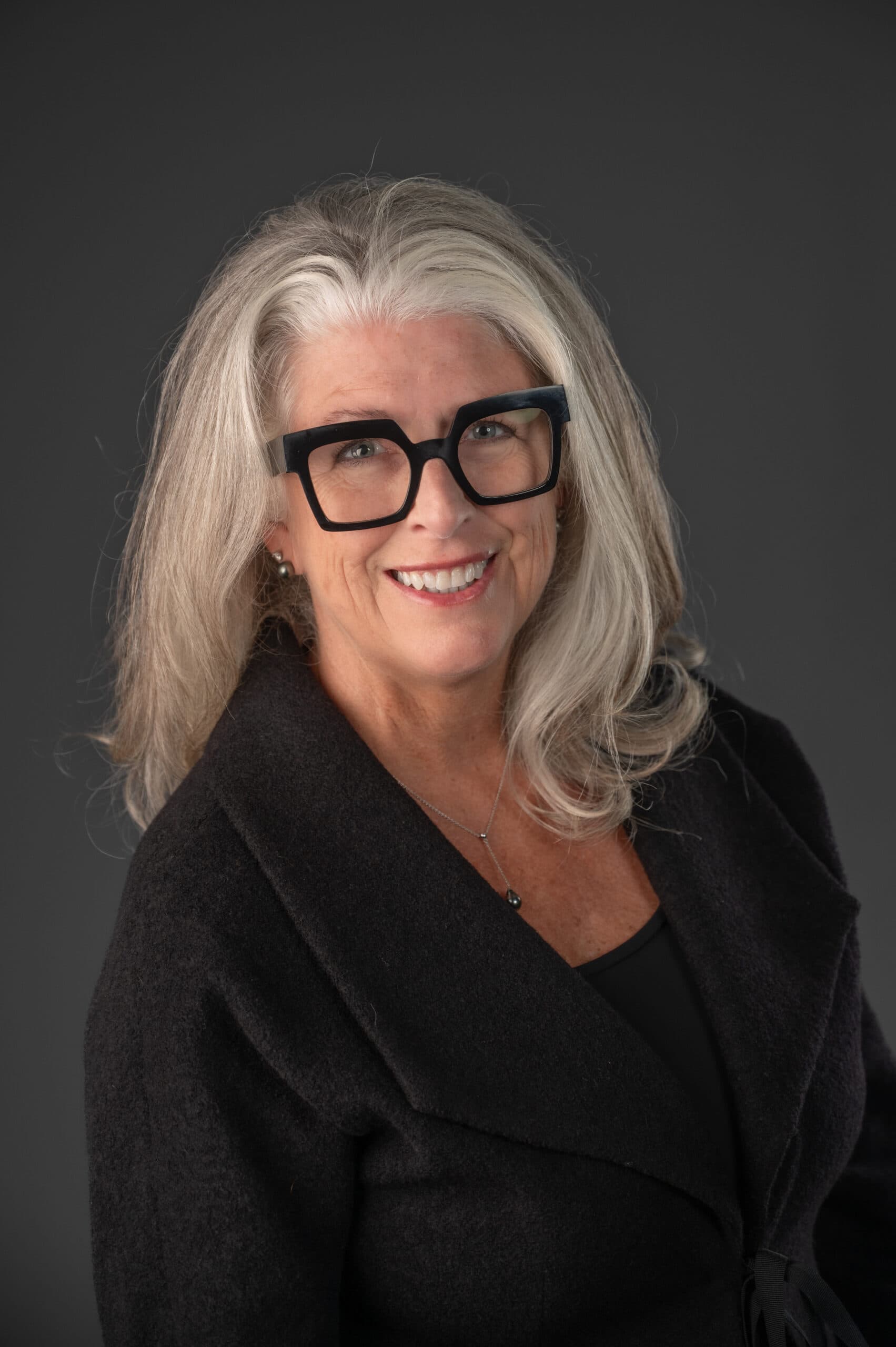Lisa Berry Headshot wearing black with a grey background and glasses on.