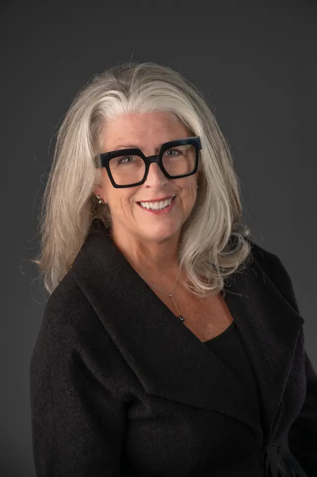 Lisa Berry Headshot wearing black with a grey background and glasses on.