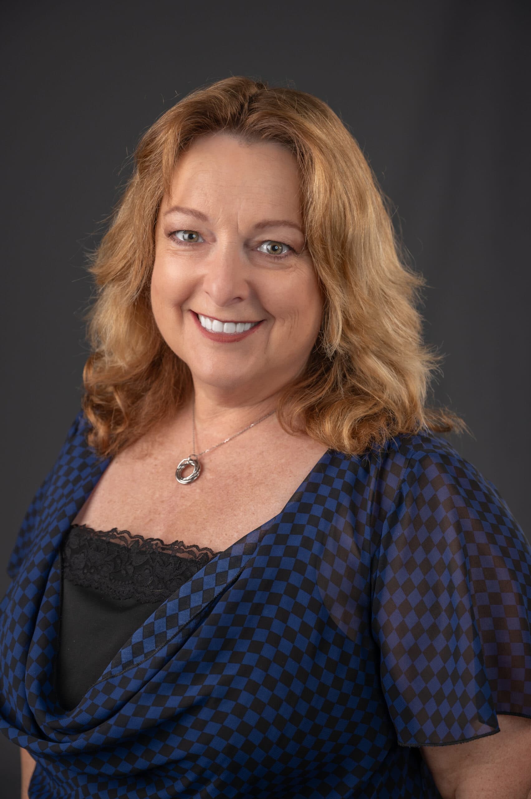 Lois Scott Brooklynn Kenney headshot smiling with grey background wearing a blue and black shirt.