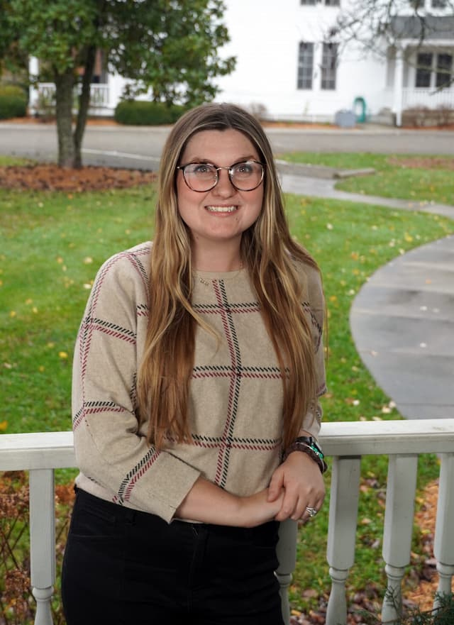 Berea College Campus Visits & Events Specialist, Brittany Dudley-Ray, leaning against a white fence, with green grass, a tree, and a white house in the background.