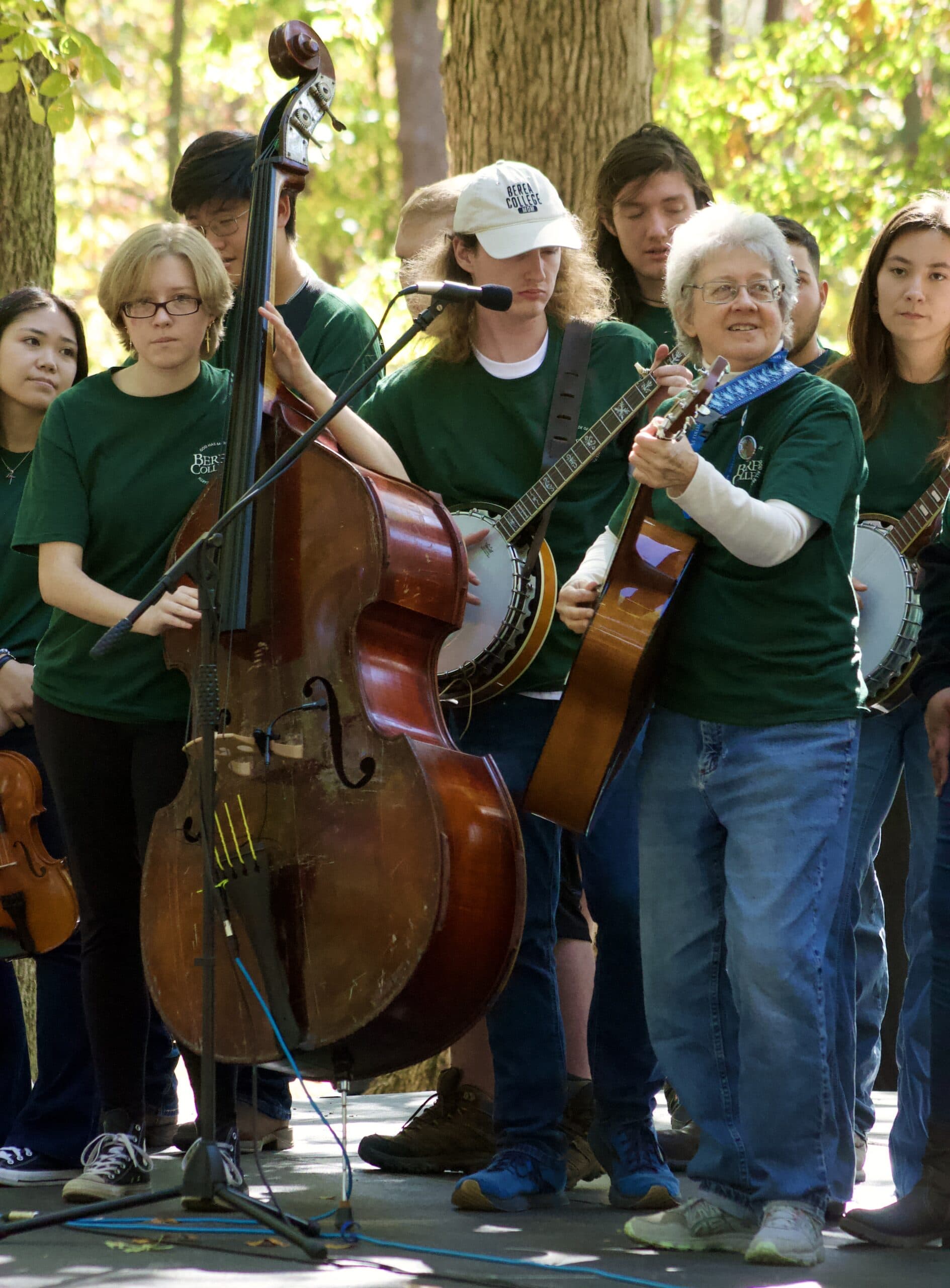 A student ensemble and their director performing outside with guitars, banjos, and upright bass.
