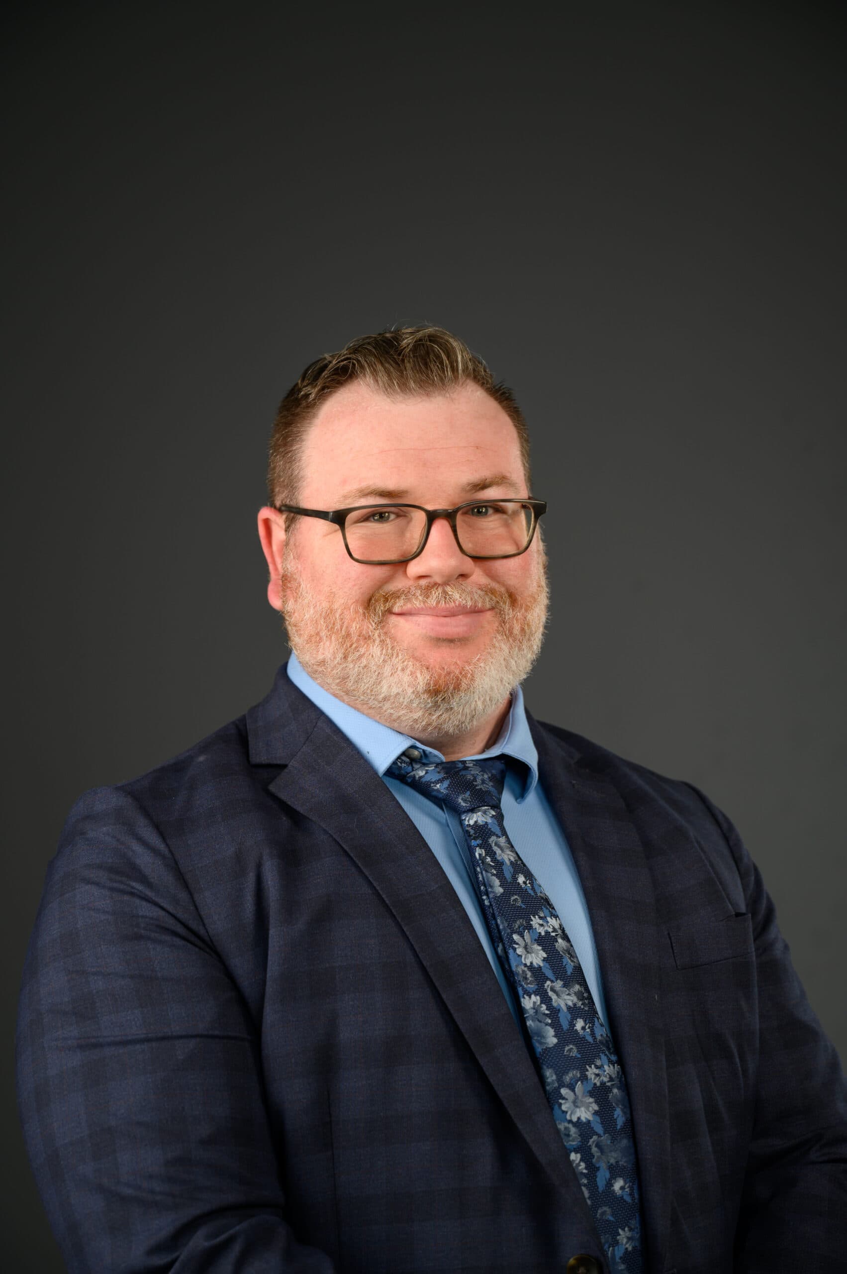 Wesley Gift headshot wearing a suit smiling and a grey background.