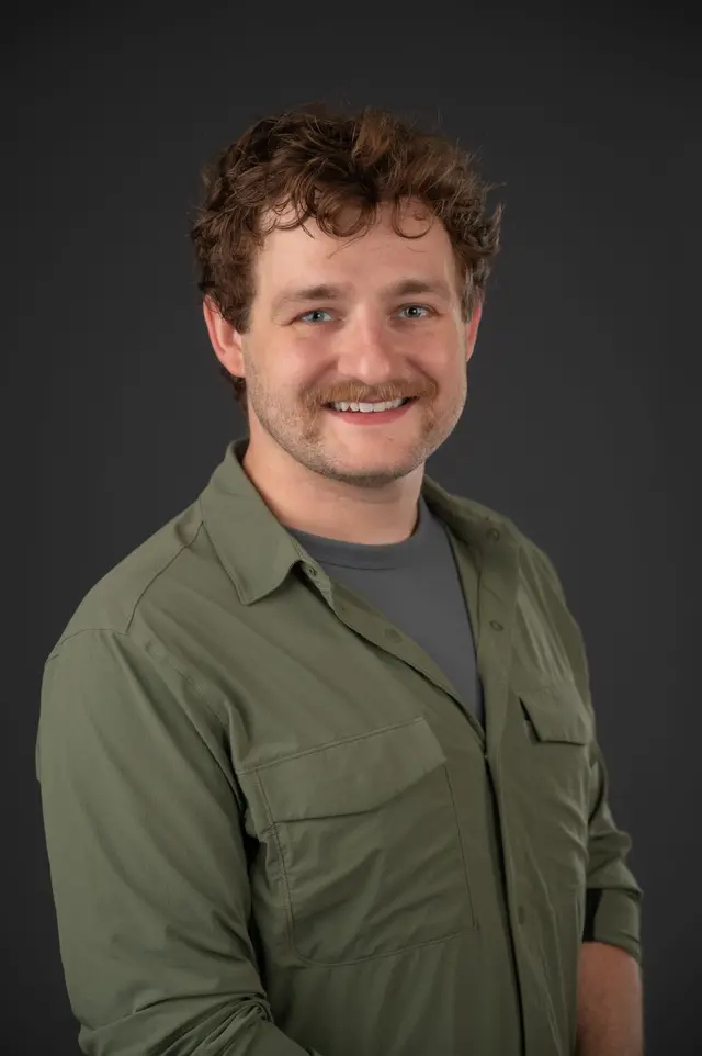 Jarrod Burgh headshot wearing a grey top and behind is a grey background.