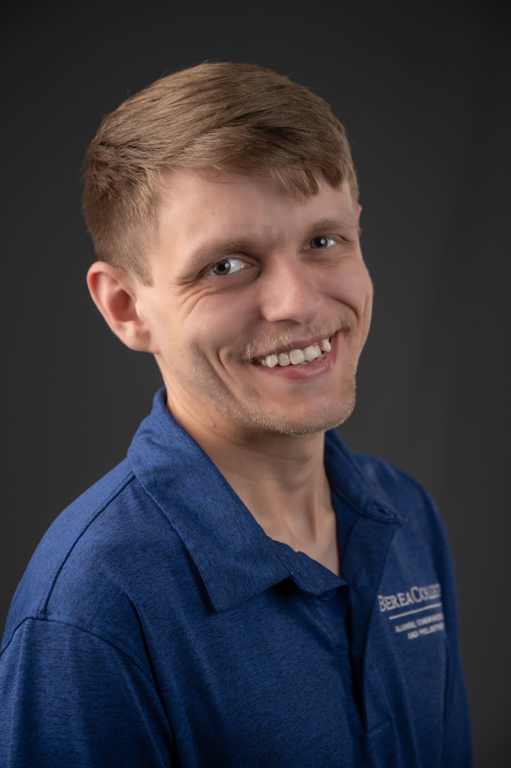 Dustin Cooper headshot smiling towards the camera wearing a blue top and a grey background.