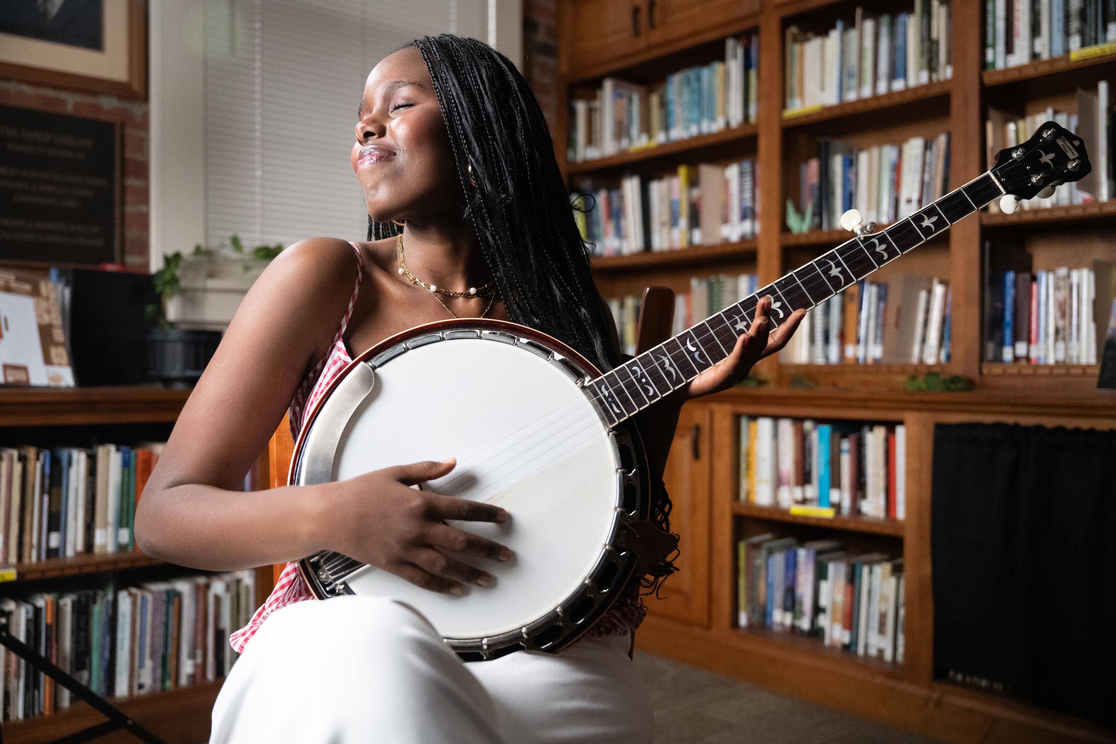 A sitting woman smiles to herself while holding a banjo as if she is about to play.