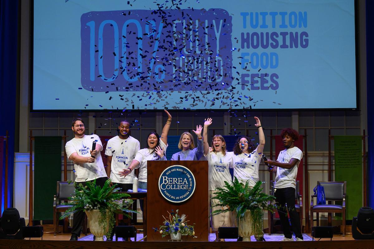 A celebratory photo of Dr. Cheryl Nixon, President of Berea College accompanied by Berea students on the Phelps Stokes stage at Opening Convocation 2026. Blue confetti is seen popped in the air, as the students are cheering, moments after Dr. Nixon announces the Financial Freedom Pledge.